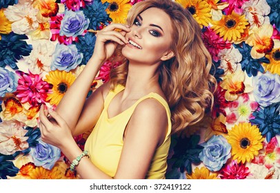 Beautiful sensual woman in yellow dress and bracelet on colorful wall of flowers. Fashion photo, nice hair