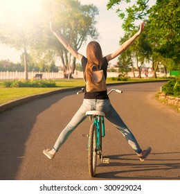 Beautiful Sensuality Elegance Red Hair Back Woman Cyclist, Has Black Shirt, Blue Jeans. Has Slim Sport Body And Ass. Motion On Great Bicycle In Urban City. Portrait Nature Amazing Sunset. Quest