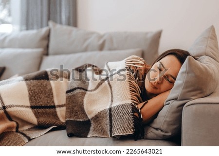 Beautiful serene woman sleeping on comfy sofa under warm cozy plaid in modern living room. Healthy daytime nap, tiredness relief, repose and relaxation during day, lazy weekend at home.