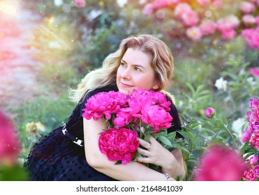 Beautiful And Serene Young Woman Hugging A Bright Bouquet Of Pink Peonies. Background - A Garden, Rays Of The Sun, A Peony Field. Flowers And Floristry Concept