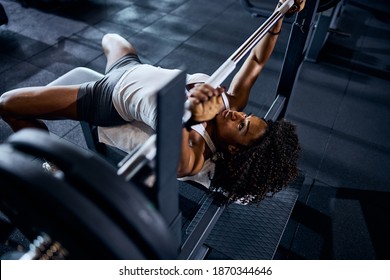 Beautiful serious focused curly-haired young female bodybuilder doing the bench press exercise at the gym - Powered by Shutterstock