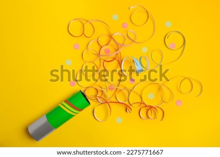 Beautiful serpentine and confetti bursting out of party popper on yellow background, flat lay