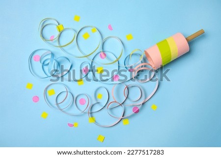 Beautiful serpentine and confetti bursting out of party popper on light blue background, flat lay