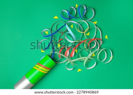 Beautiful serpentine and confetti bursting out of party popper on green background, flat lay