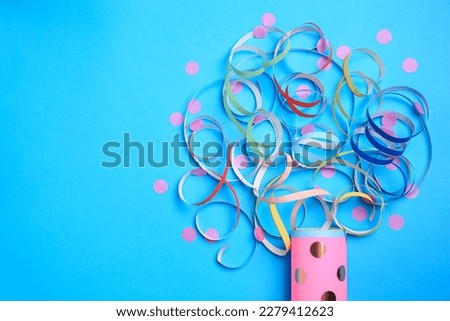 Beautiful serpentine and confetti bursting out of party popper on light blue background, flat lay. Space for text