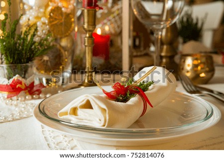 Beautiful served table with decorations, candles and lanterns. Little gingerbread house with glaze on white tablecloth. Living room decorated with lights and Christmas tree. Holiday setting close up. 
