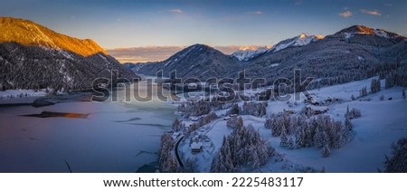 The beautiful setting of the Weissensee Nature Park. Frozen Lake Weissensee, Carinthia, Alps, Austria. Aerial drone shot in January 2022. Sunset time.