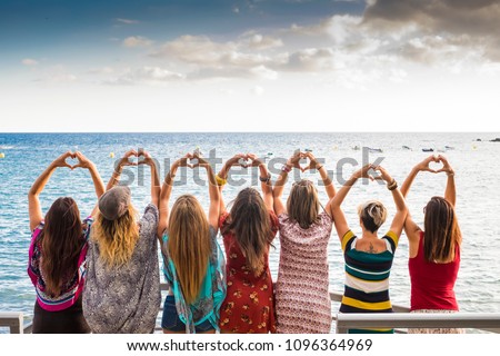 beautiful seven girls from the backside doing a heart with the hands looking at the ocean waiting the sunset in vacation leisure activity. friendship all together forever concept travel to sea party