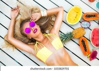 Beautiful sexy blonde girl in pool at hotel. Yellow swimsuit glasses tropical fruit papaya watermelon pineapple, summer vacation, smiling, close-up on top, blue water, slender figure