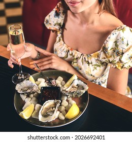 Beautiful sexy brunette woman in expensive restaurant eating oysters and drinking champagne. Eat out concept, oysters and champagne in a restaurant, eat and drink.