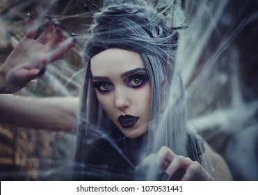 Beautiful sexy Gothic girl with pale skin and long white hair like spider black widow in spider web. Dark Princess with long vampire claws in the crown. Spider woman weaving net. Gothic look.