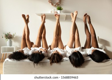 Beautiful sexy multiethnic girls best friends wear bathrobes lying on bed in row raise legs up celebrate bridal shower bachelorette spa party together, epilation depilation feet skin beauty concept