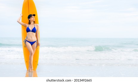 Beautiful Sexy Surfer Asian Woman On The Beach At Sunset, Posing With Yellow Surf Board. Island Summer Holiday Attractive Woman And Her Hobby. Lifestyle.