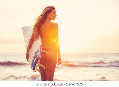 Beautiful sexy surfer girl on the beach at sunset