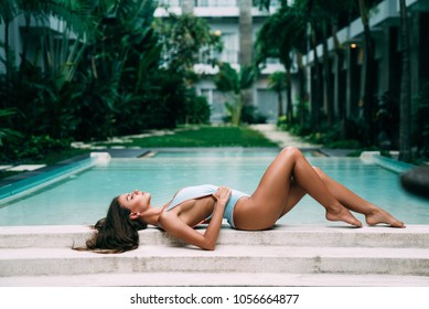 Beautiful sexy woman model in blue bikini lies near swimming pool, posing and tanned on summer vacation. Healthy body care.