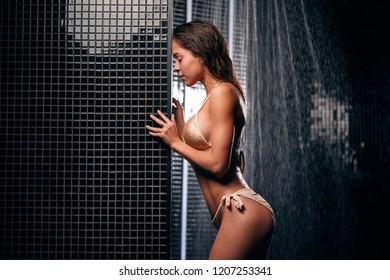 Beautiful Sexy Woman With Tanned Skin Taking Shower In Spa Bathroom. Portrait Of Fashion Model Girl Indoors Over Black Shimmering Background.