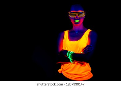 Beautiful sexy woman with UV face paint, glowing clothing, glowing bracelet in front of camera, half body shot, confident look. Asian woman. Party concept.