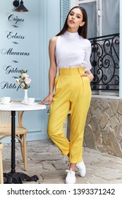 Beautiful sexy woman wear fashion summer collection clothes casual style blouse yellow trousers slim body pretty face model accessory jewelry brunette hair bread shop cafe breakfast morning coffee.