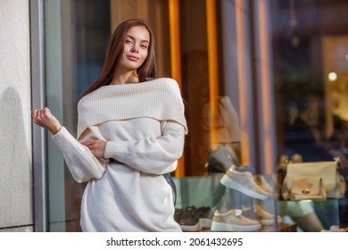 Beautiful Sexy Woman Wearing Fashionable Spring Or Fall Clothes  - White Warm Fluffy Sweater Dress. Outdoors Female Model In Stylish Elegant Outfit Posing In Street Look In Camera. Copy  space Blurred