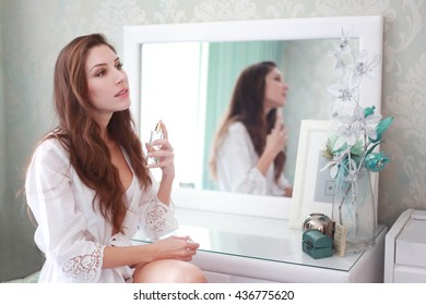 Beautiful Sexy Young Woman Sitting Near The Mirror At Her Bedroom And Use Perfume On Her Neck.