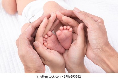 Beautiful shape hands of father, mother, hold tiny newborn baby feet leg on white bed with love, care, family safety and protection concept