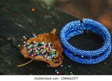 Beautiful, shiny, color bracelet with large beadwork beads. On a special stand for jewelry. Beads are scattered on a wooden table - Powered by Shutterstock