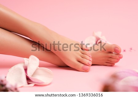 Beautiful shoot of female hands and feet on pink background surrounded by magnolia pink flowers.