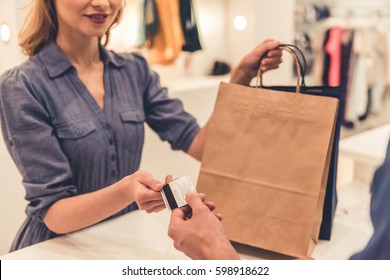 Beautiful shop assistant is smiling while giving purchases and credit card to handsome client