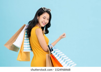 Beautiful Shopaholic Asian Woman Carrying Shopping Bags In Light Blue Background With Copy Space For Sale And Discount Concepts