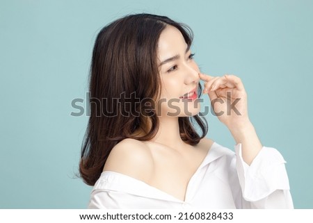 Beautiful short hair asian woman model touch her nose and clean fresh skin on blue background. Face care, Facial treatment, Cosmetology, beauty and spa, Women portrait.