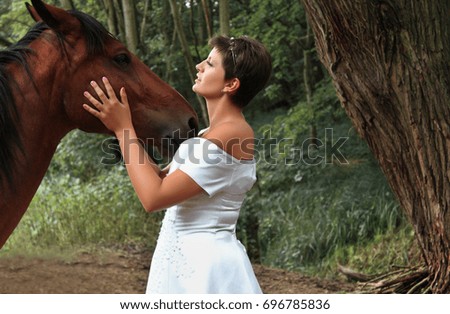 Beautiful short haired woman touching to horse head forest background