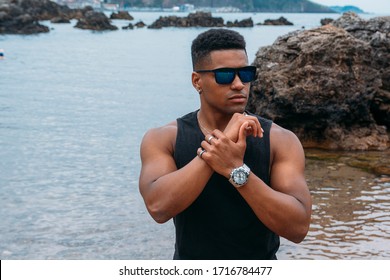 A beautiful shot of an attractive man with sunglasses with the rocks and the ocean in the background
