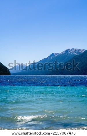 A beautiful shot of the calm clear sea surrounded by greenery-covered hills and mountains