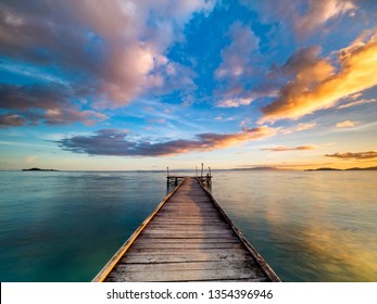 Beautiful shot of a long jetty/pier at sunset. Minimal image with jetty in the center stretching to the ocean. Warm sunset tones of orange, yellow, pink, blue and purple. Smooth water and reflection