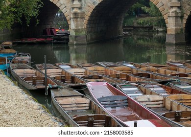 A beautiful shot of many Punts moored up at the Head of the River with green water near an arc bridge