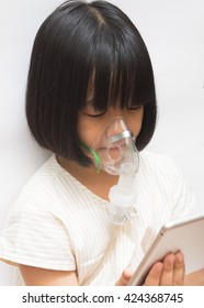 Beautiful Sick Girl Inhalation Therapy By The Mask Of Inhaler Playing Ipad Tablet While Curing . Close Up Image Of A Cute Kid With Respiratory Problem Or Asthma.
