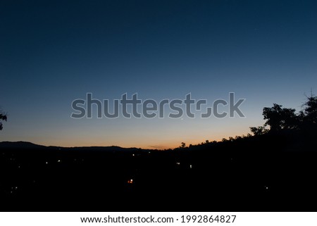 Beautiful silhouette picture of waxing crescent moon in orange, dark blue sky and houses lights illuminating.