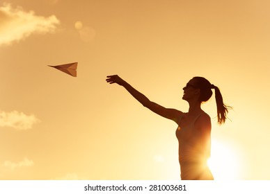 Beautiful Silhouette Of Young Woman Throwing Paper Airplane.