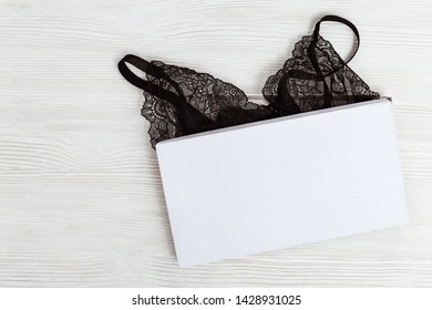 Beautiful silk lace bra for woman in paper box. Black fashionable lingerie. Glamorous stylish sexy lace lingerie in giftbox on white background. Flat lay. Copy space. Mock-up. 