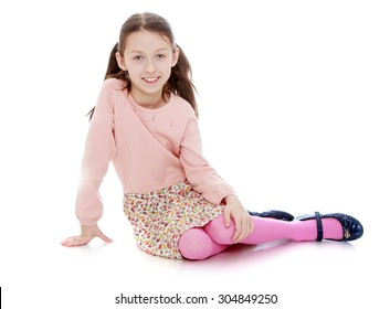 Beautiful Skinny Little Girl With Long Hair Braided In Pigtails Is Sitting On The Floor. -Isolated On White Background