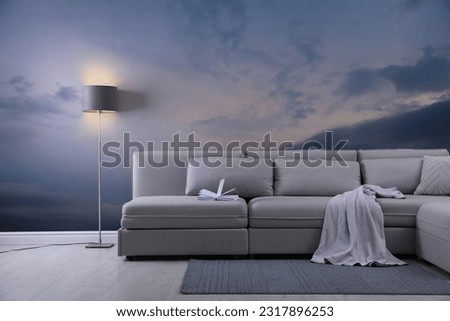 Beautiful sky with clouds as wallpaper pattern. Living room interior with comfortable sofa near wall