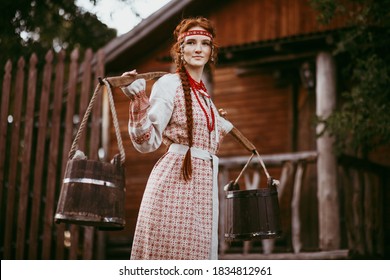 Beautiful Slavic girl with long blonde hair and brown eyes in a white and red embroidered suit and a yoke on her shoulders.Traditional clothing of the Ukrainian region. - Shutterstock ID 1834812961