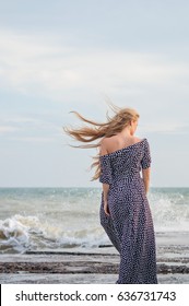 beautiful slender blonde in a long polka-dot dress on a background of azure sea. portrait from the back

