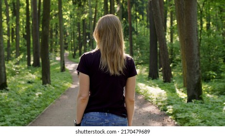 beautiful slender blonde woman walks through woods and turns to camera with smile. happy lady in black T-shirt walks through park, turn around and looks at camera with satisfied look. Summer sunny day