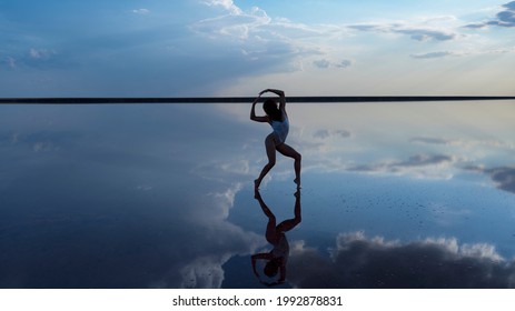 Beautiful slender dancer performs a dance movement in the reflection of the sky in the water