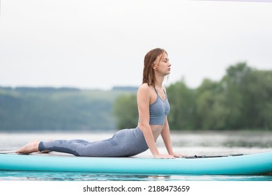Beautiful slender girl doing yoga on a paddleboard. A young woman does water sports in the summer sunrise.