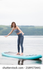 Beautiful slender girl doing yoga on a paddleboard. A young woman does water sports in the summer sunrise.