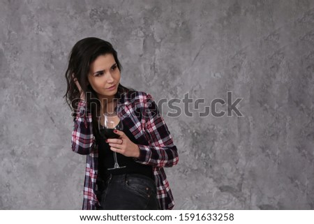 Beautiful slender girl with short dark hair in a burgundy checkered shirt with a glass of red wine in a lofts gray interior style
