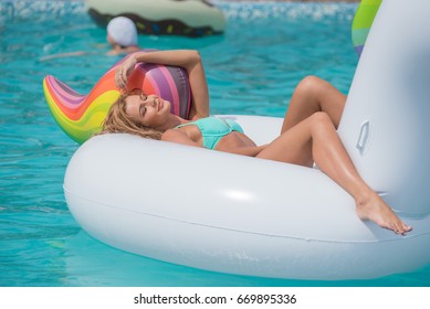 beautiful slim girl in a swimsuit. Floating on a big white beach inflatable unicorn pool