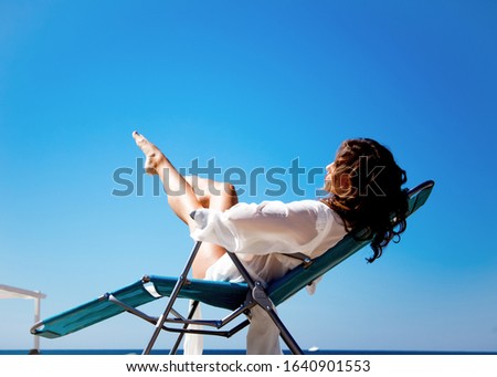 Beautiful slim girl wearing white swimwear posing on deck chair at the background send beach and sea at summer. Stanning woman relaxing on the vacation. skin cair concept